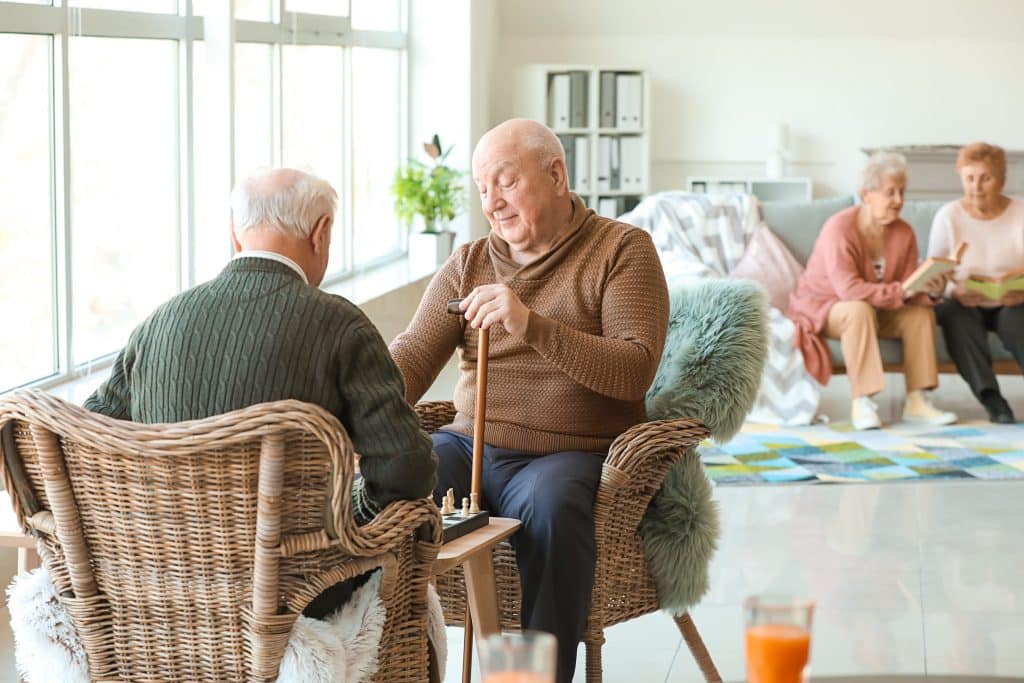 Senior men playing chess in a home-like setting.