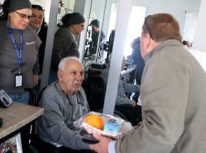 An older man in a wheelchair accepts a lunch from another man.