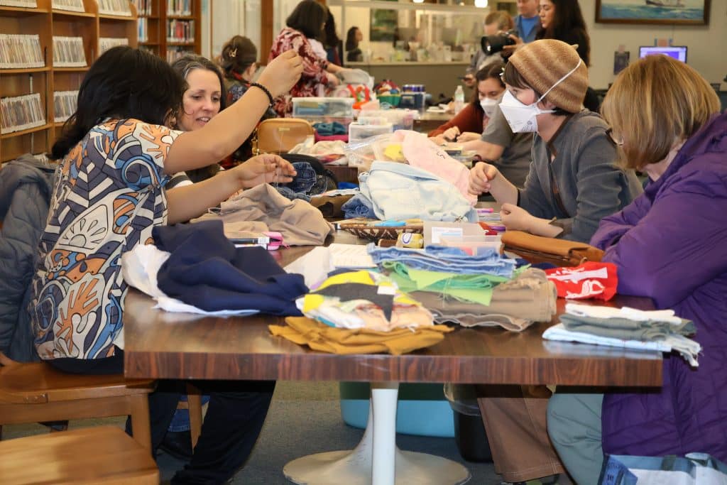 People sit at a library table sewing clothing.