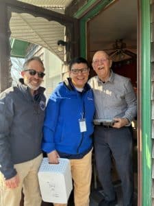 A man and woman pose with an older man in his doorway as they deliver his luncheon meal.